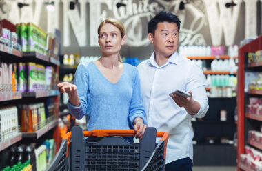 Confused international couple, woman and Asian man walking in supermarket. They spread their hands