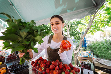 Young saleswoman at work, holding parsley and tomato in hands