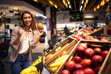 Positive brunette woman holding coconut at grocery store fruit d